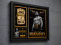 A framed UFC memorabilia display mounted on a gray wall. The black shadowbox frame contains a beige UFC glove on the left, a black-and-gold poster of Islam Makhachev on the right, and a small match-card style insert at the bottom left.